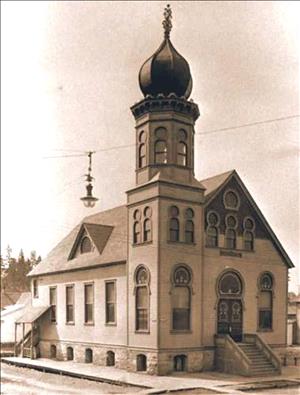 Photo of Temple Emanu-El in Spokane, a wooden building on a stone foundation with gabled roof and a tower on one corner topped by an onion-shaped dome